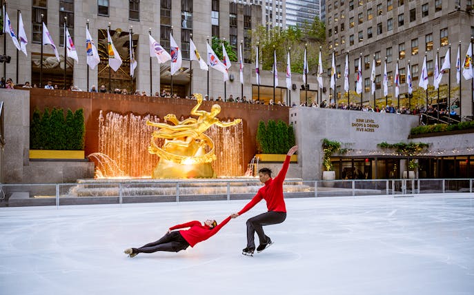 Ice skaters performing at Rockefeller Center's The Rink with Prometheus statue in the background.
