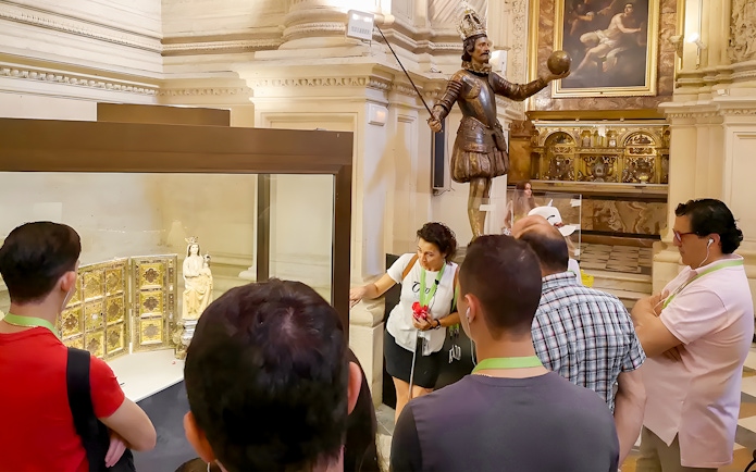 Tourists with guide viewing Seville Cathedral exhibit featuring religious artifacts.