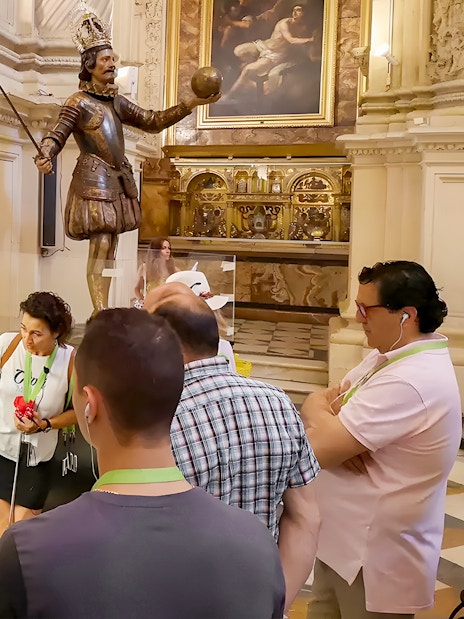 Tourists with guide viewing Seville Cathedral exhibit featuring religious artifacts.