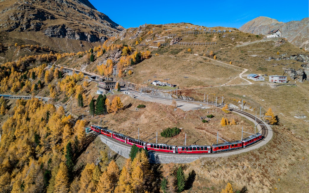 Bernina Express train winding through autumnal Swiss Alps towards Tirano.