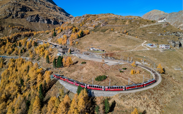 Bernina Express train winding through autumnal Swiss Alps towards Tirano.