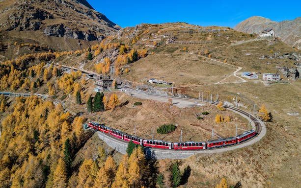 Bernina Express train winding through autumnal Swiss Alps towards Tirano.
