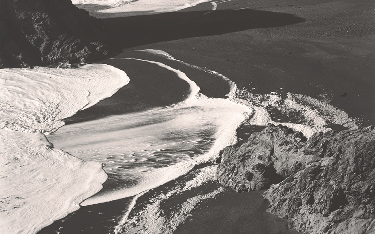 Black and white photograph of ocean waves on a rocky shore, part of an exhibit at Fundación MAPFRE Madrid.