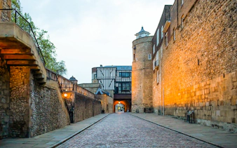 Tower of London cobblestone path at dusk, leading to historic archway.