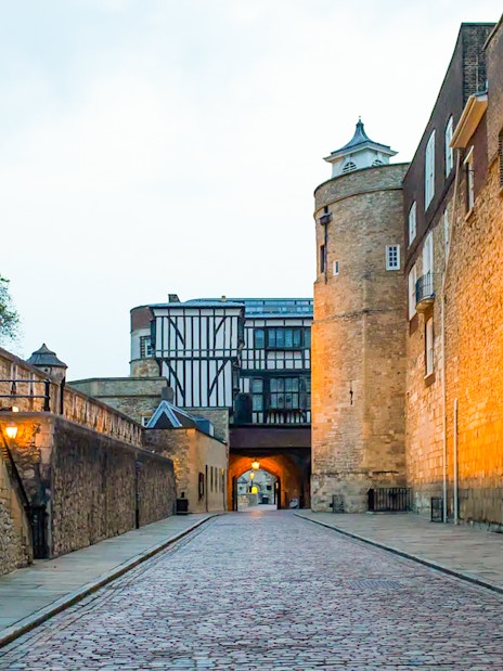 Tower of London cobblestone path at dusk, leading to historic archway.