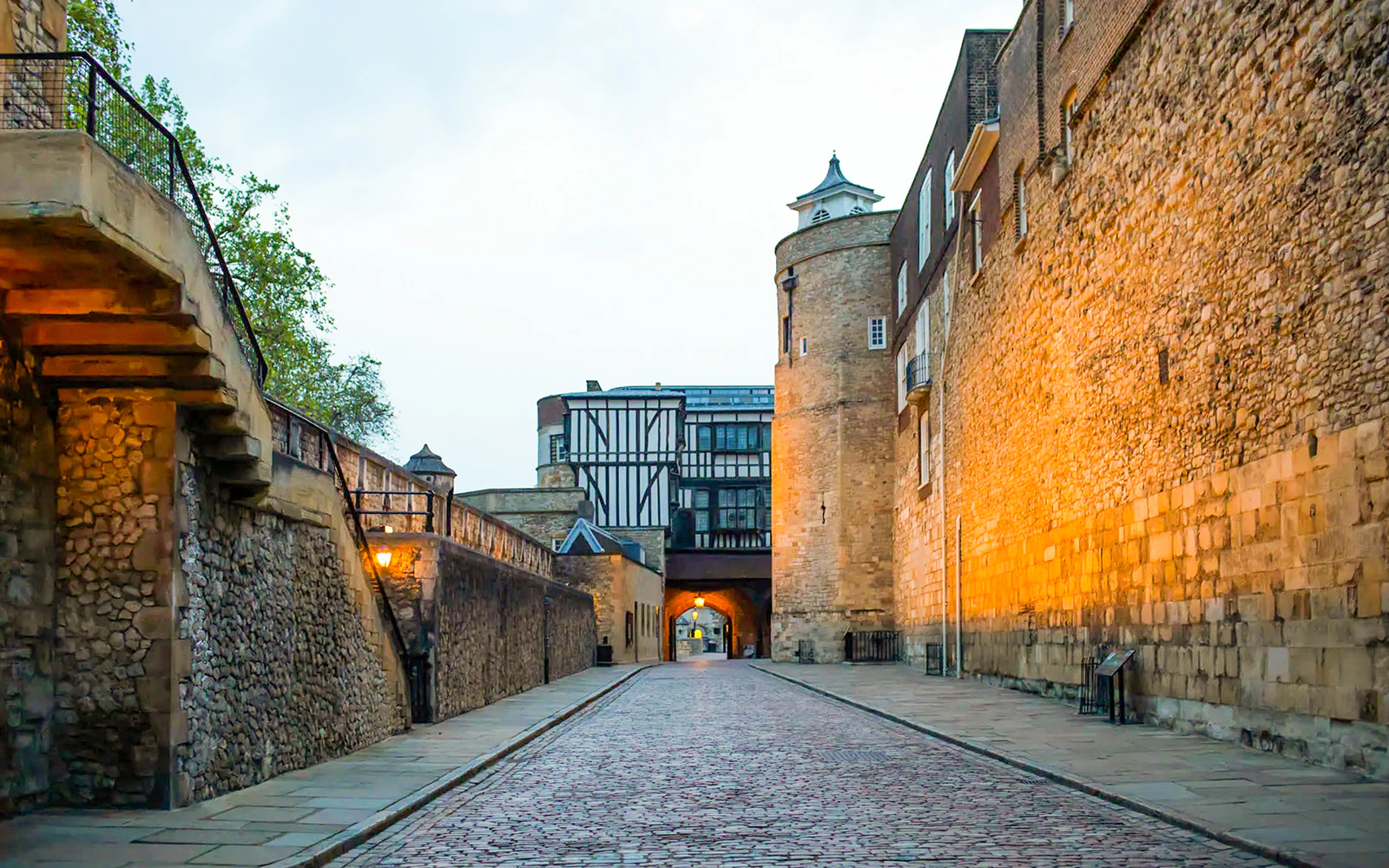 Tower of London cobblestone path at dusk, leading to historic archway.