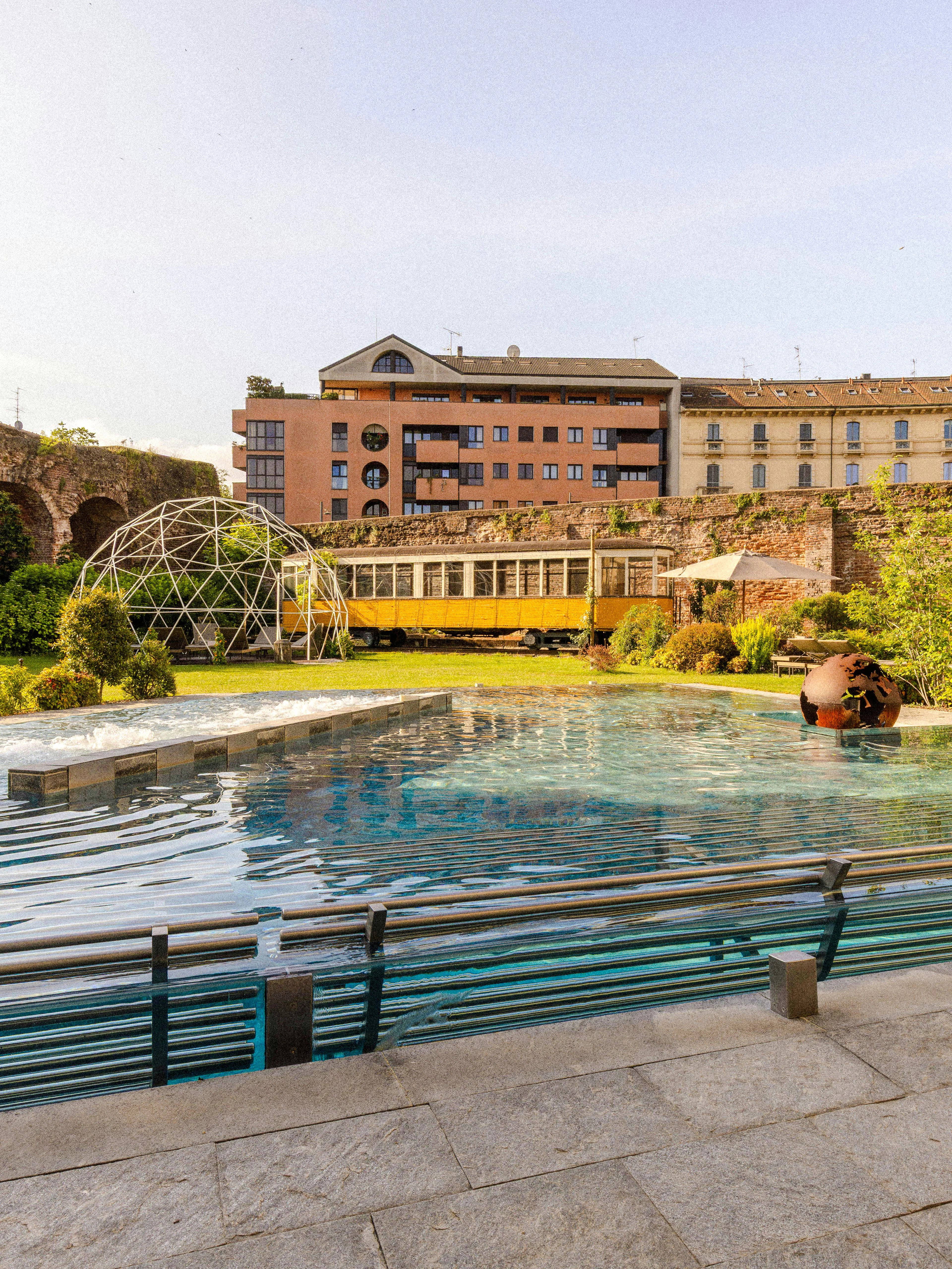 Outdoor pool and garden area at QC Terme spa in Milan with historic architecture.