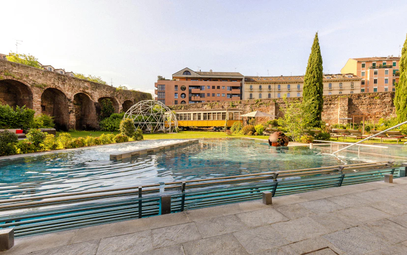 Outdoor pool and garden area at QC Terme spa in Milan with historic architecture.