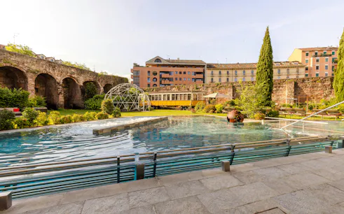 Outdoor pool and garden area at QC Terme spa in Milan with historic architecture.