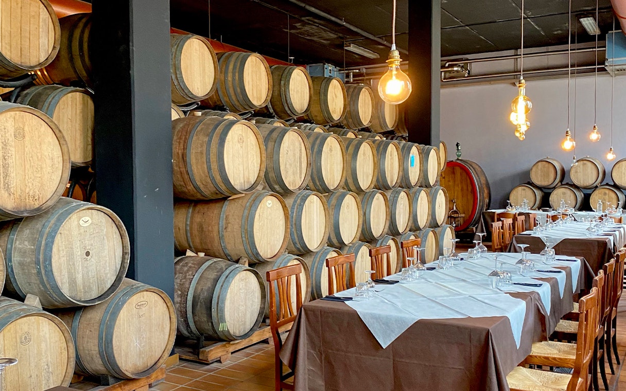 Chianti winery tasting room with wooden barrels and set dining tables.