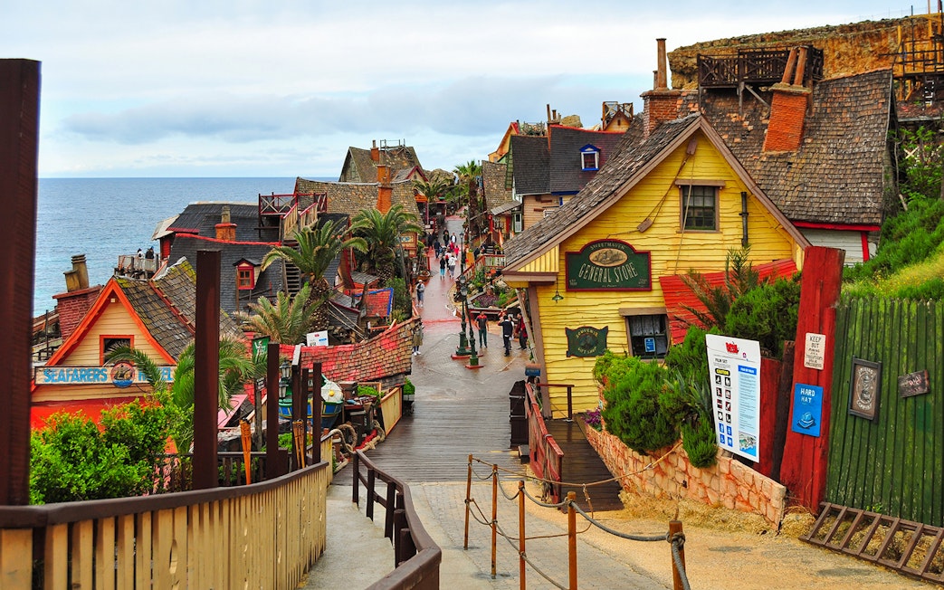 Street view of colorful wooden buildings in Popeye Village, Malta, near the sea.