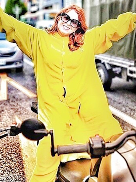 Woman in yellow onesie on go-kart with arms outstretched on Tokyo street.