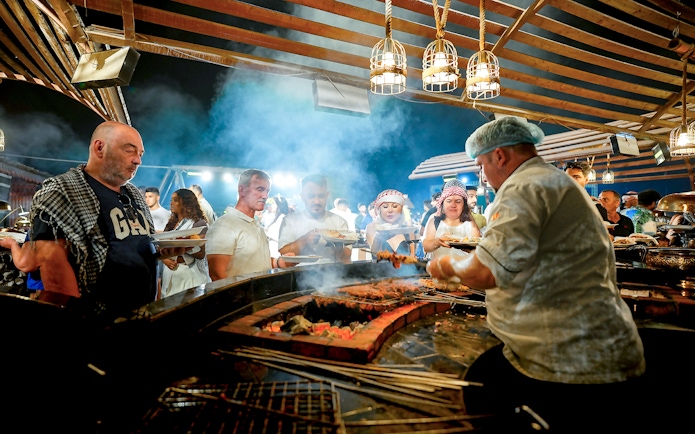 Chef serving buffet food at desert safari experience with guests in line.