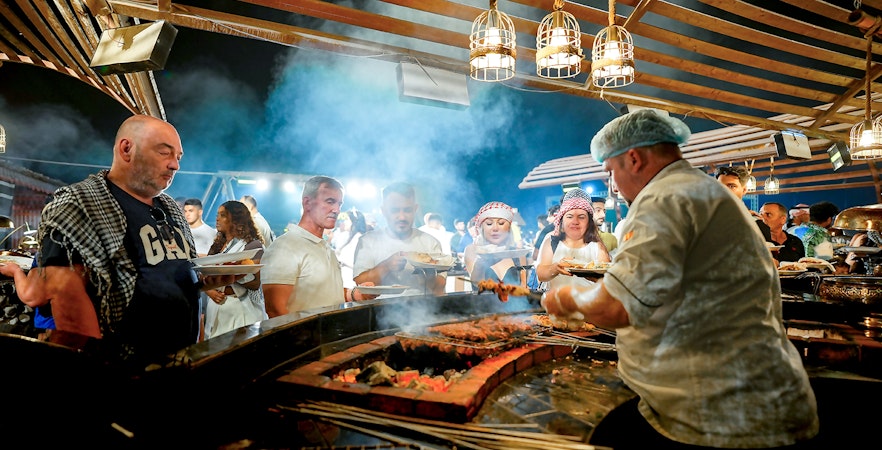 Chef serving buffet food at desert safari experience with guests in line.