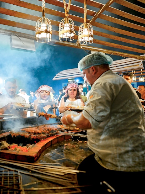 Chef serving buffet food at desert safari experience with guests in line.