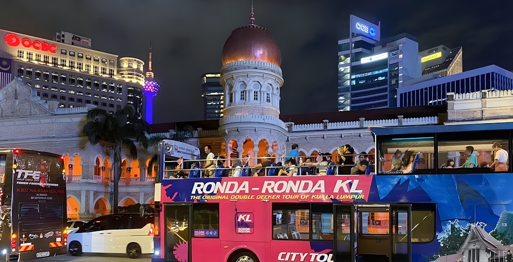 Kuala Lumpur night bus tour passing Sultan Abdul Samad Building with city lights.