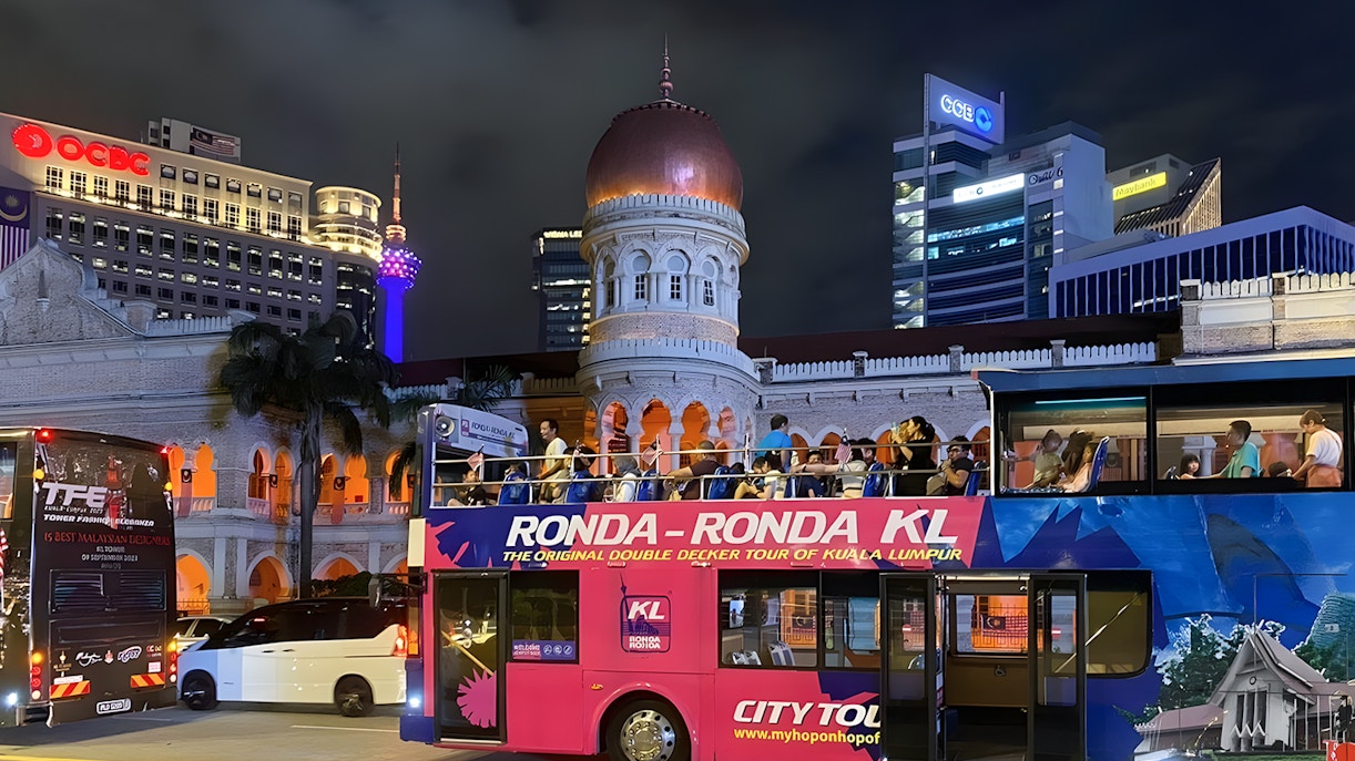 Kuala Lumpur night bus tour passing Sultan Abdul Samad Building with city lights.