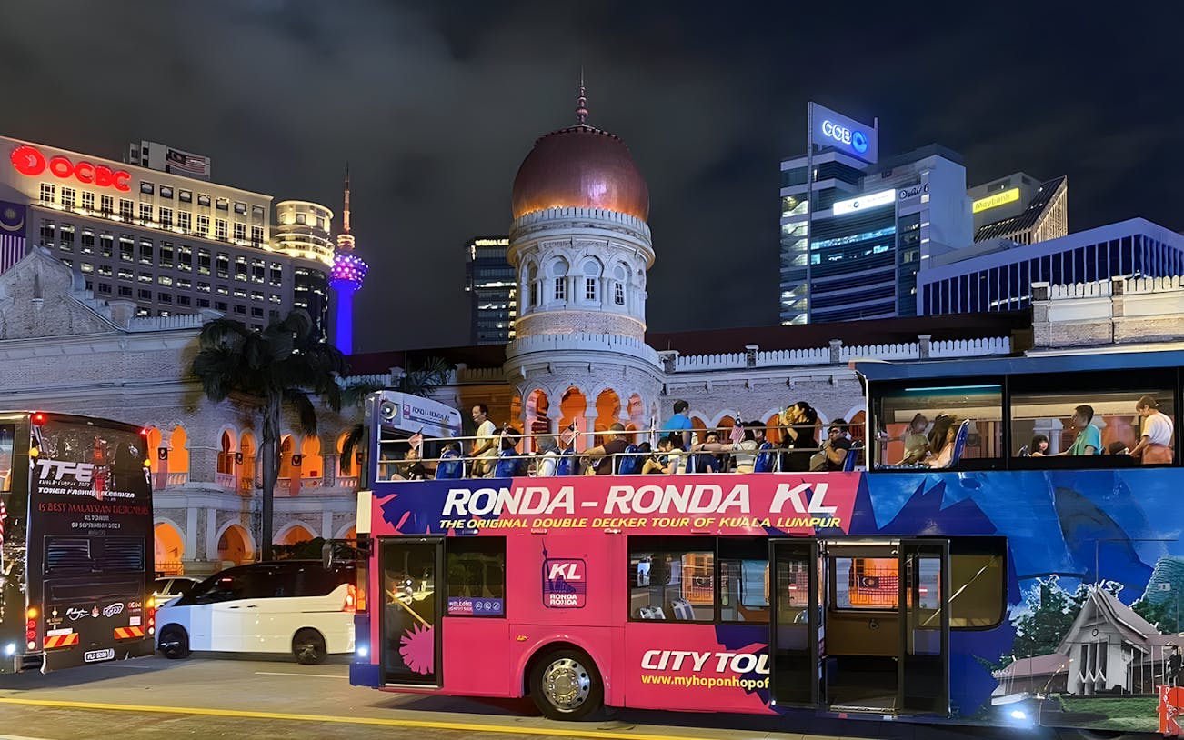 Kuala Lumpur night bus tour passing Sultan Abdul Samad Building with city lights.