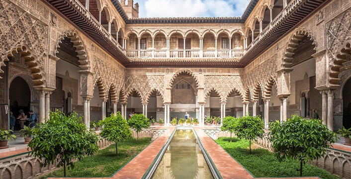 Alcazar of Seville courtyard with intricate arches and reflecting pool.