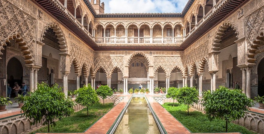 Alcazar of Seville courtyard with intricate arches and reflecting pool.