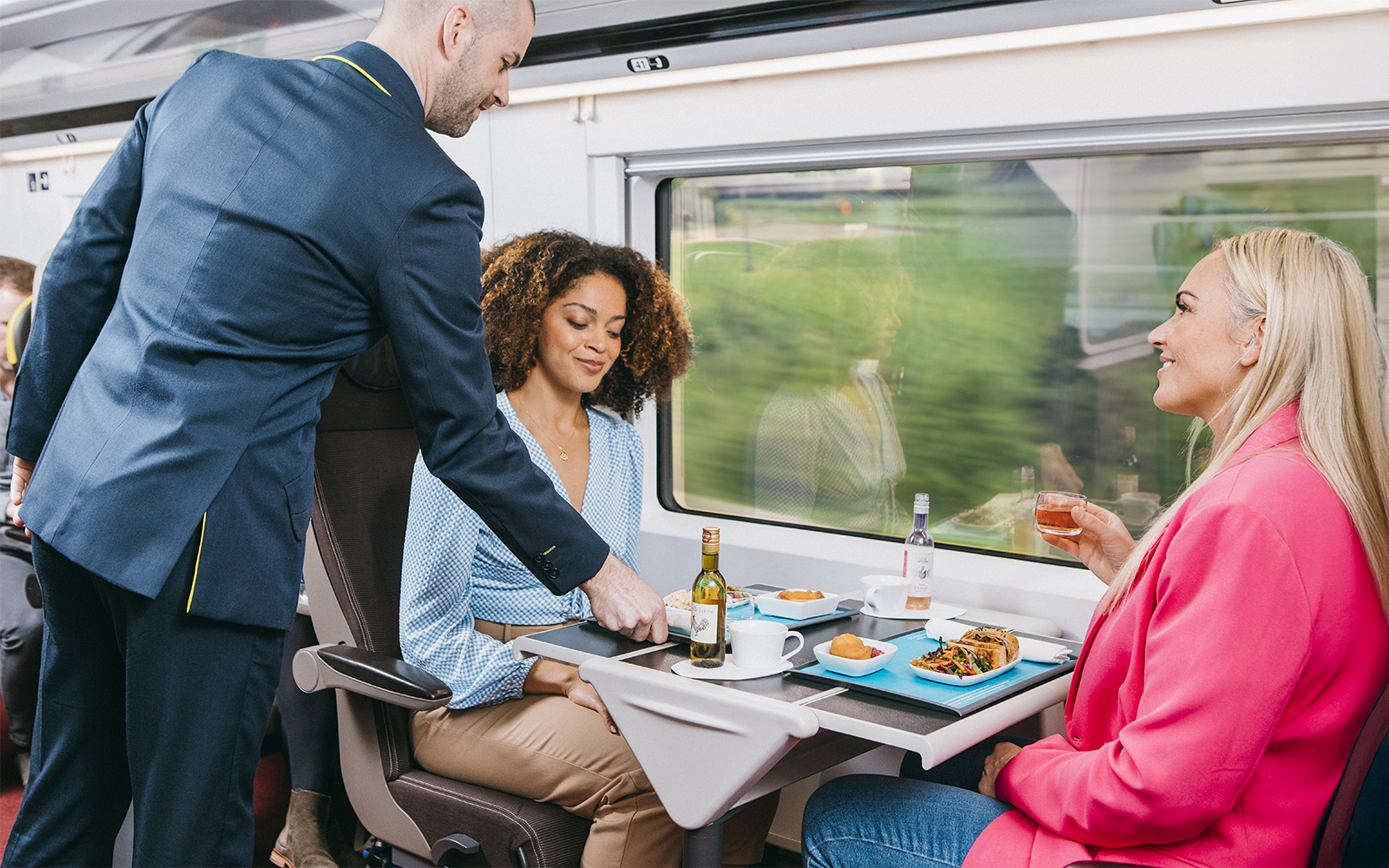 Train attendant serving meals to passengers on Eurostar train journey.