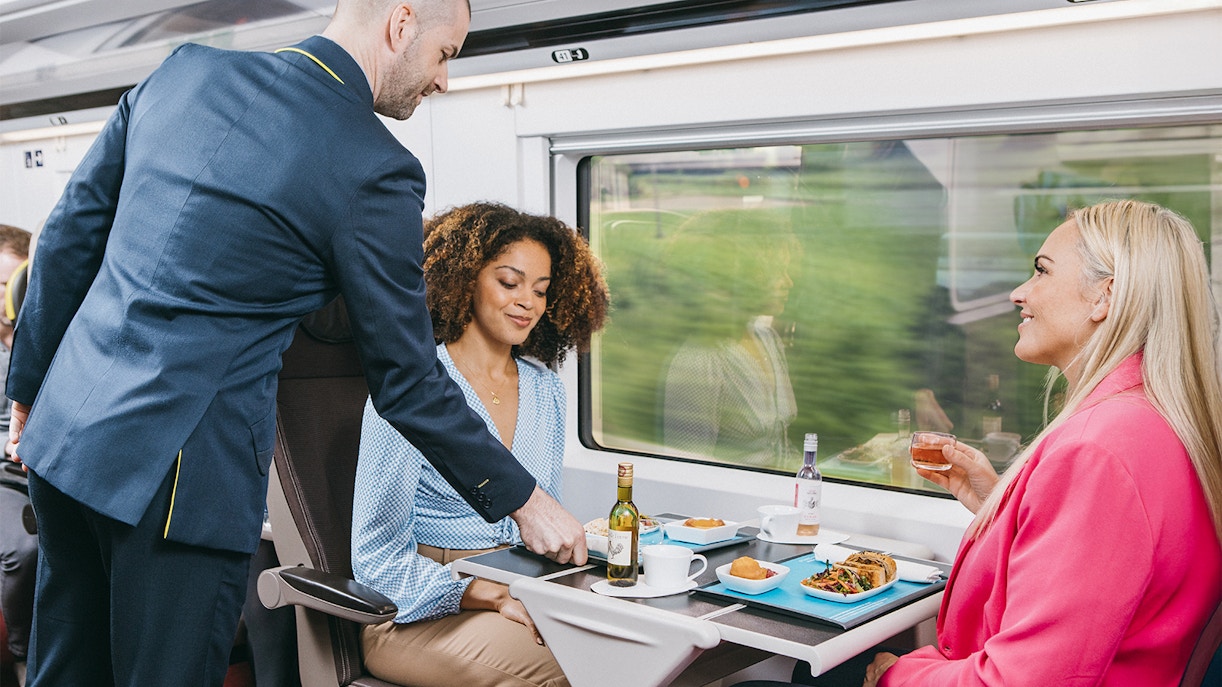 Train attendant serving meals to passengers on Eurostar train journey.