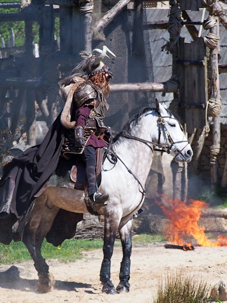 Medieval knight on horseback at Puy du Fou with fire in the background.