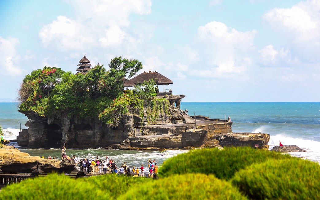 Tanah Lot Temple on a rocky outcrop with tourists and ocean backdrop in Bali, Indonesia.