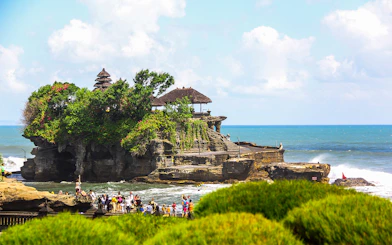 Tanah Lot Temple on a rocky outcrop with tourists and ocean backdrop in Bali, Indonesia.