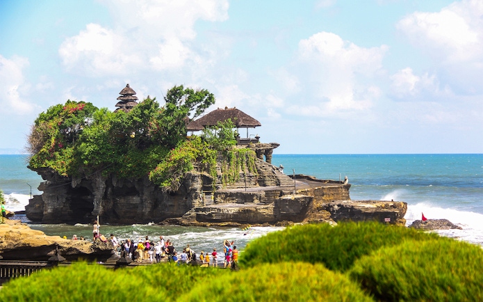 Tanah Lot Temple on a rocky outcrop with tourists and ocean backdrop in Bali, Indonesia.
