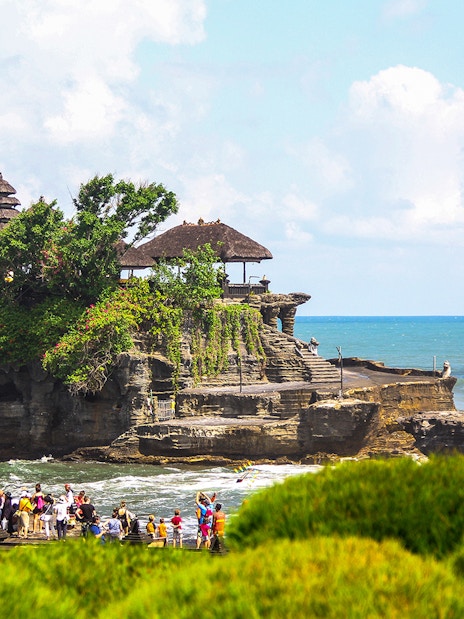 Tanah Lot Temple on a rocky outcrop with tourists and ocean backdrop in Bali, Indonesia.