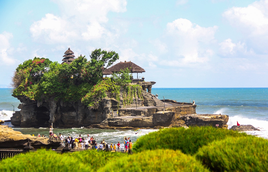 Tanah Lot Temple on a rocky outcrop with tourists and ocean backdrop in Bali, Indonesia.