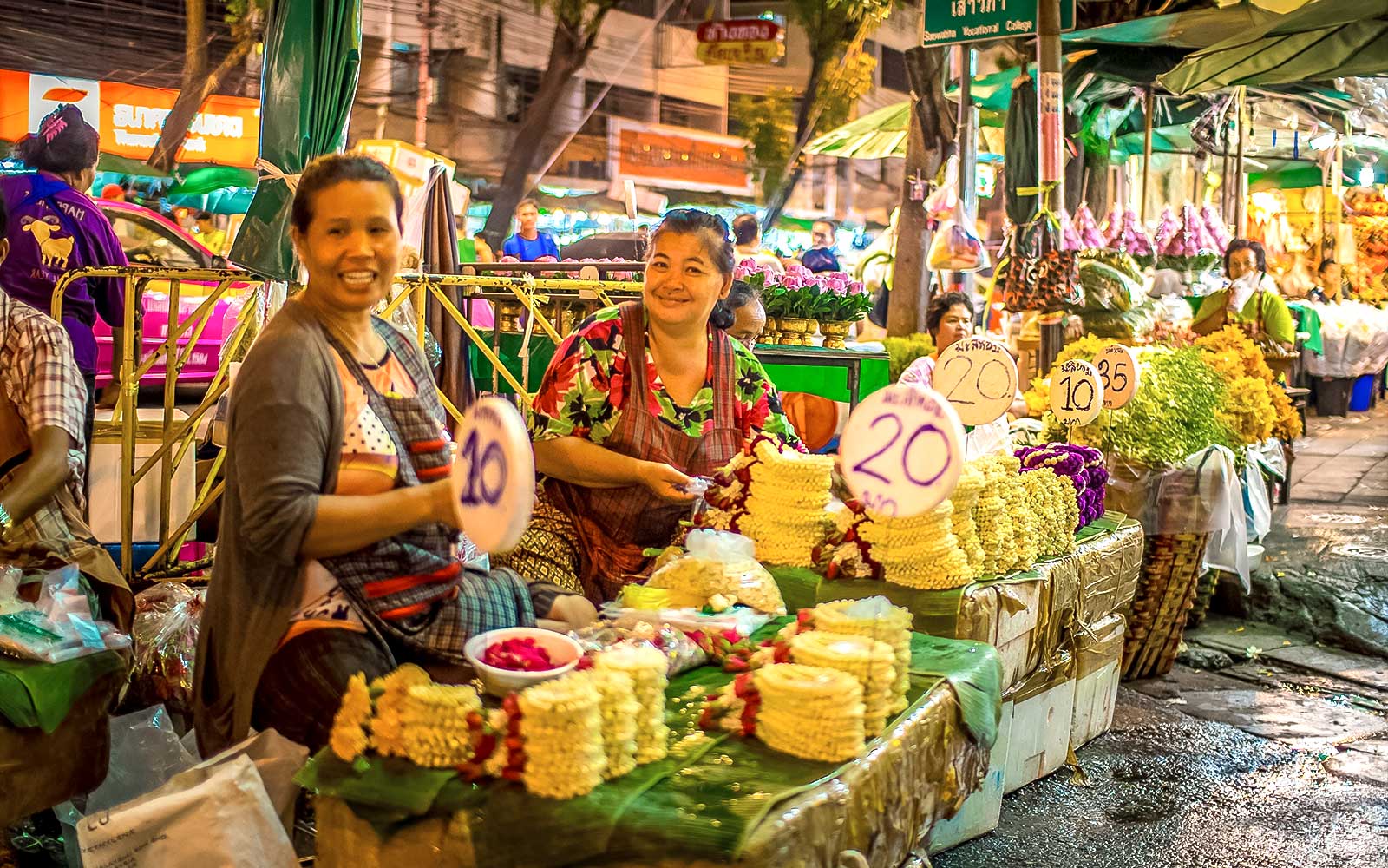 Street vendors selling flower garlands at a vibrant Bangkok night market.