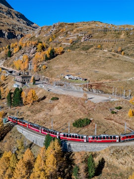 Red train traveling through Swiss Alps on a scenic route, Switzerland Interrail pass.