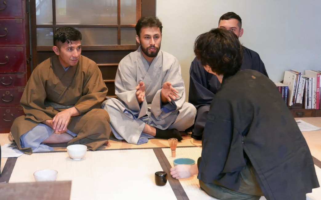 Tea ceremony participants receiving guidance in traditional Japanese room.