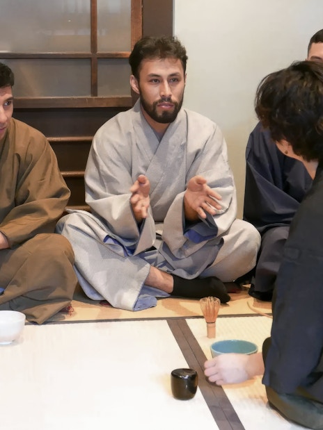 Tea ceremony participants receiving guidance in traditional Japanese room.