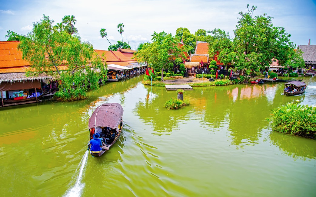 Boat navigating Ayutthaya Floating Market canal with traditional buildings and lush greenery.