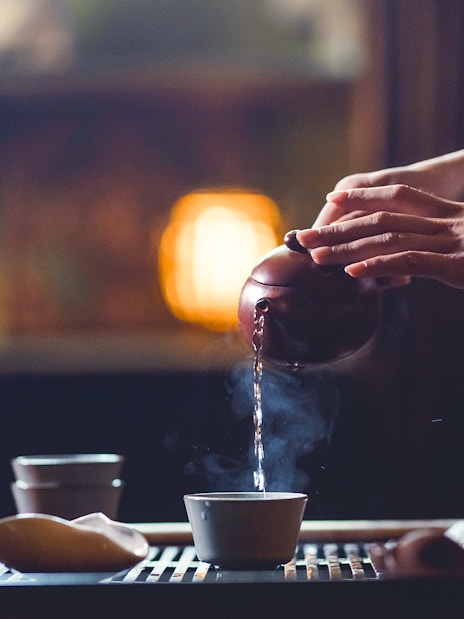 Pouring tea from a teapot into a cup with steam rising.