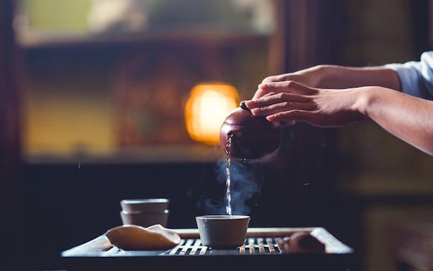 Pouring tea from a teapot into a cup with steam rising.