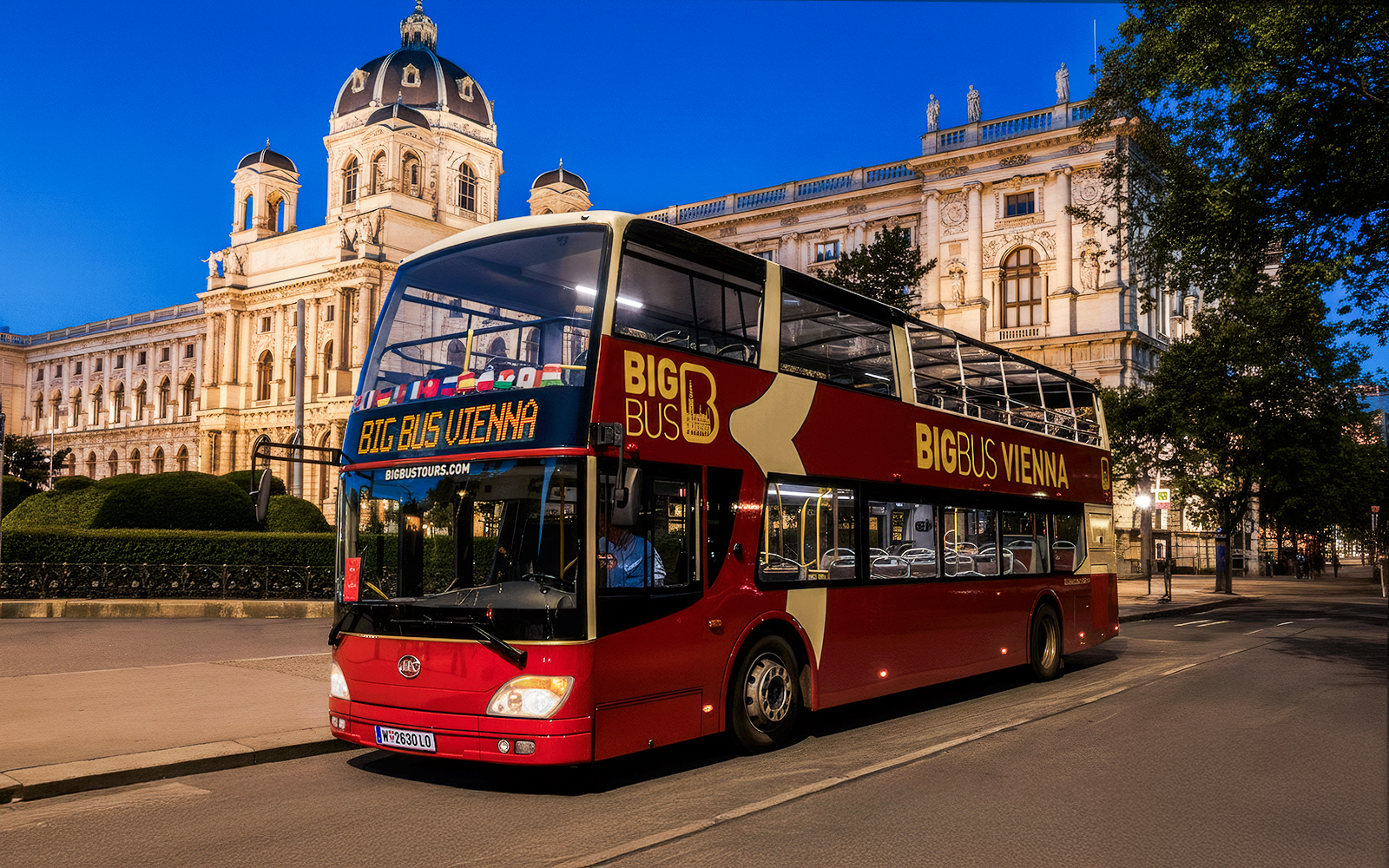 Red double-decker bus on Vienna evening tour passing historic building.