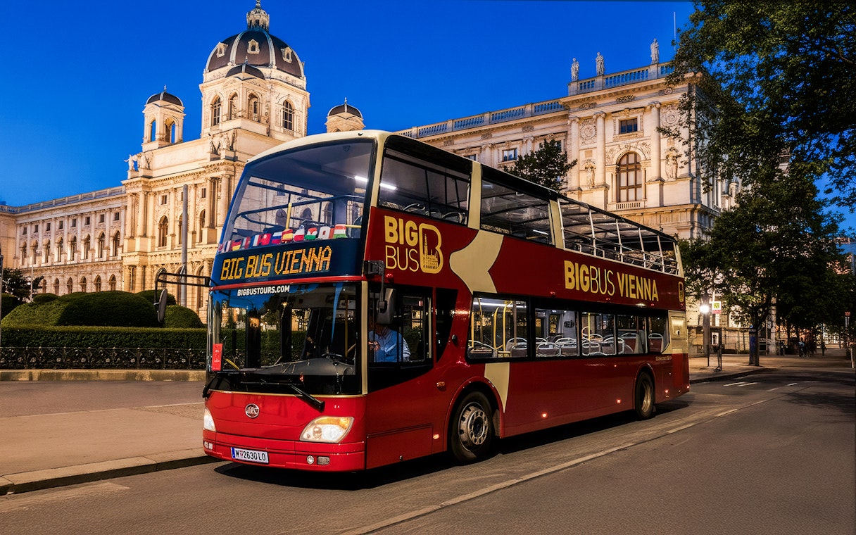 Red double-decker bus on Vienna evening tour passing historic building.