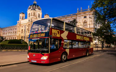 Red double-decker bus on Vienna evening tour passing historic building.