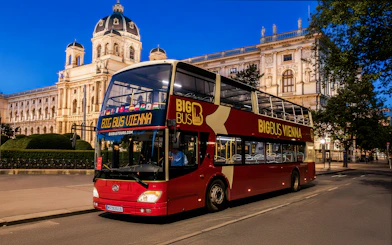 Red double-decker bus on Vienna evening tour passing historic building.