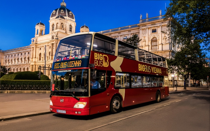 Red double-decker bus on Vienna evening tour passing historic building.