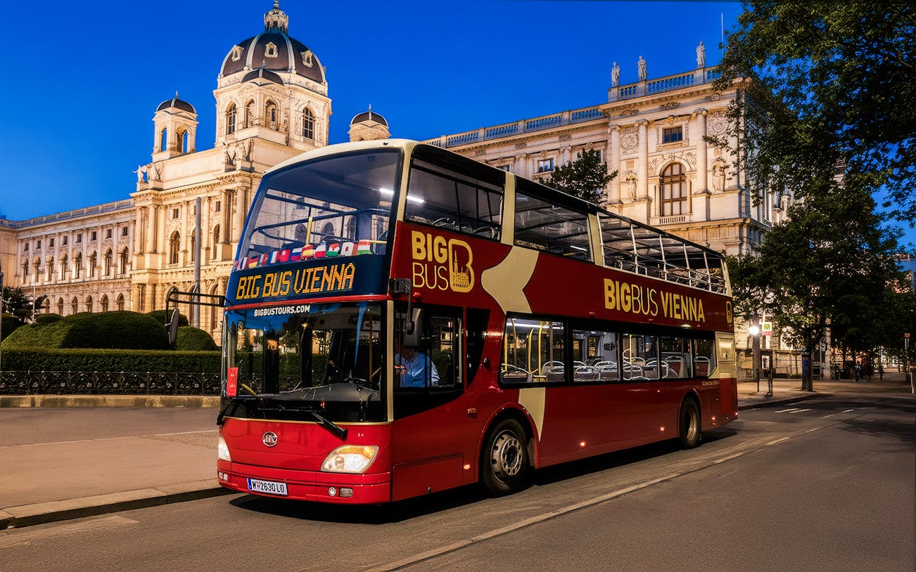 Red double-decker bus on Vienna evening tour passing historic building.