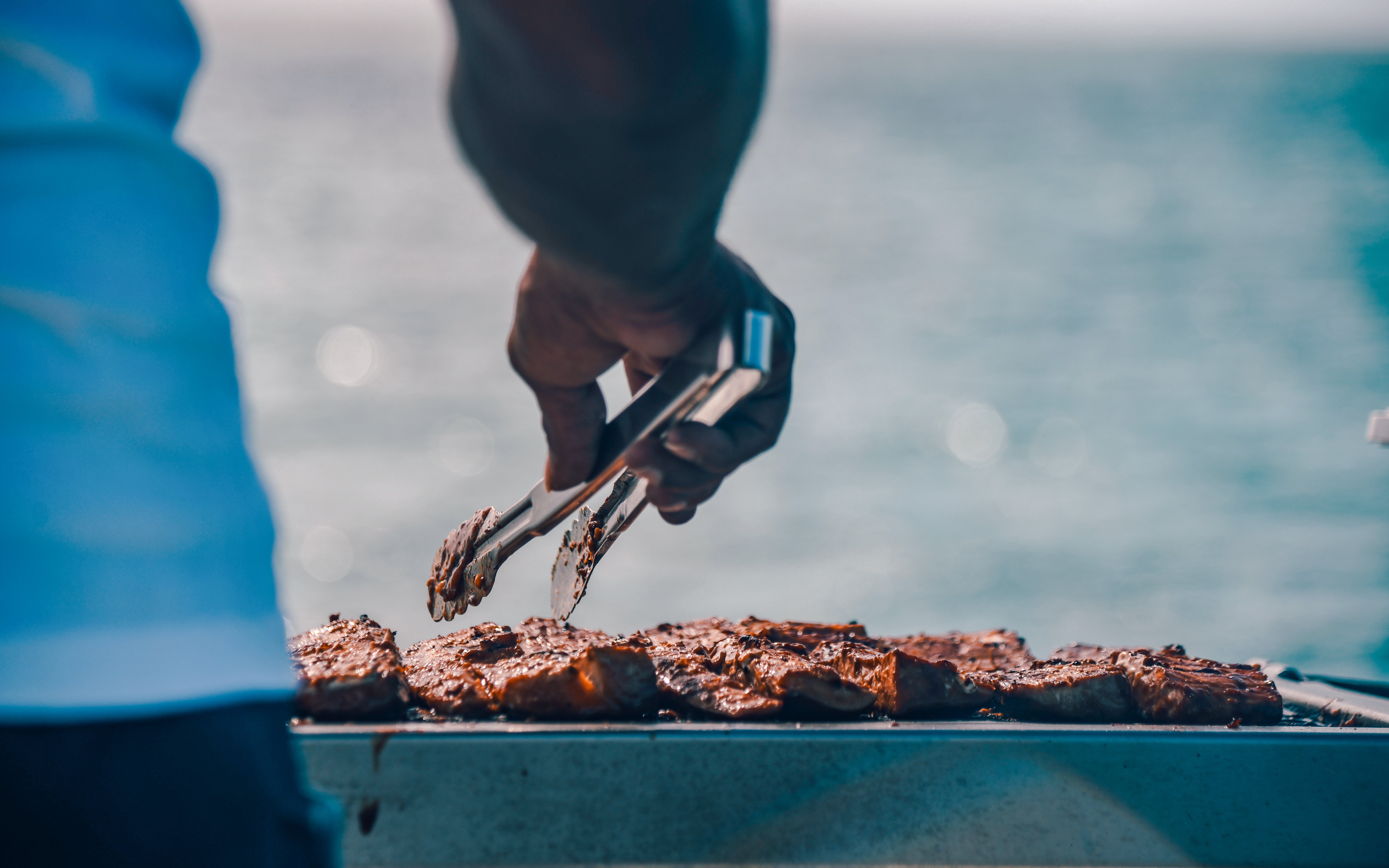 Grilling meat on a cruise boat with ocean in the background.