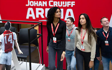 Visitors on Johan Cruijff ArenA Classic Tour wearing lanyards, near stadium seating.