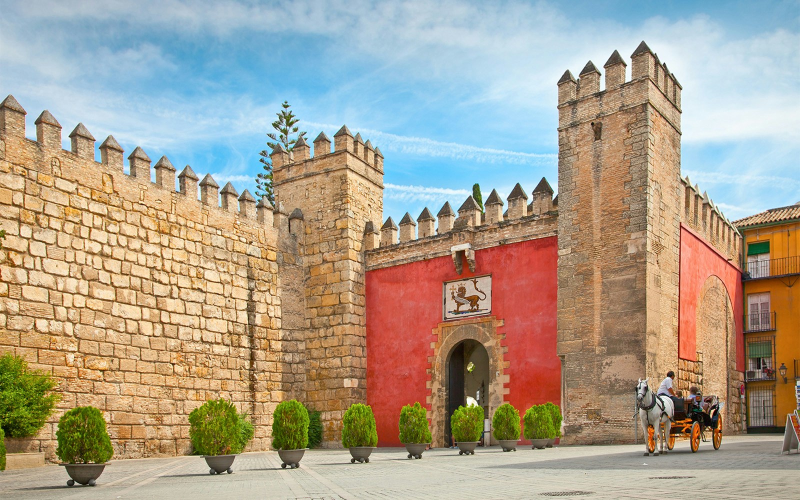 Tourists at Alcazar of Seville with Seville Cathedral and Giralda visible in the background.