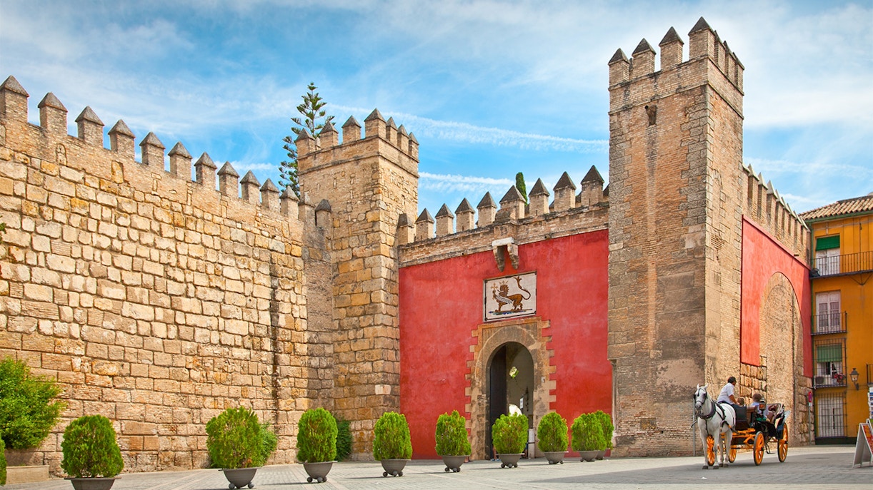 Tourists at Alcazar of Seville with Seville Cathedral and Giralda visible in the background.