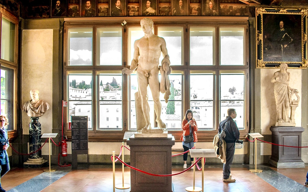 Statues and visitors inside the Uffizi Gallery, Florence, during a guided tour.